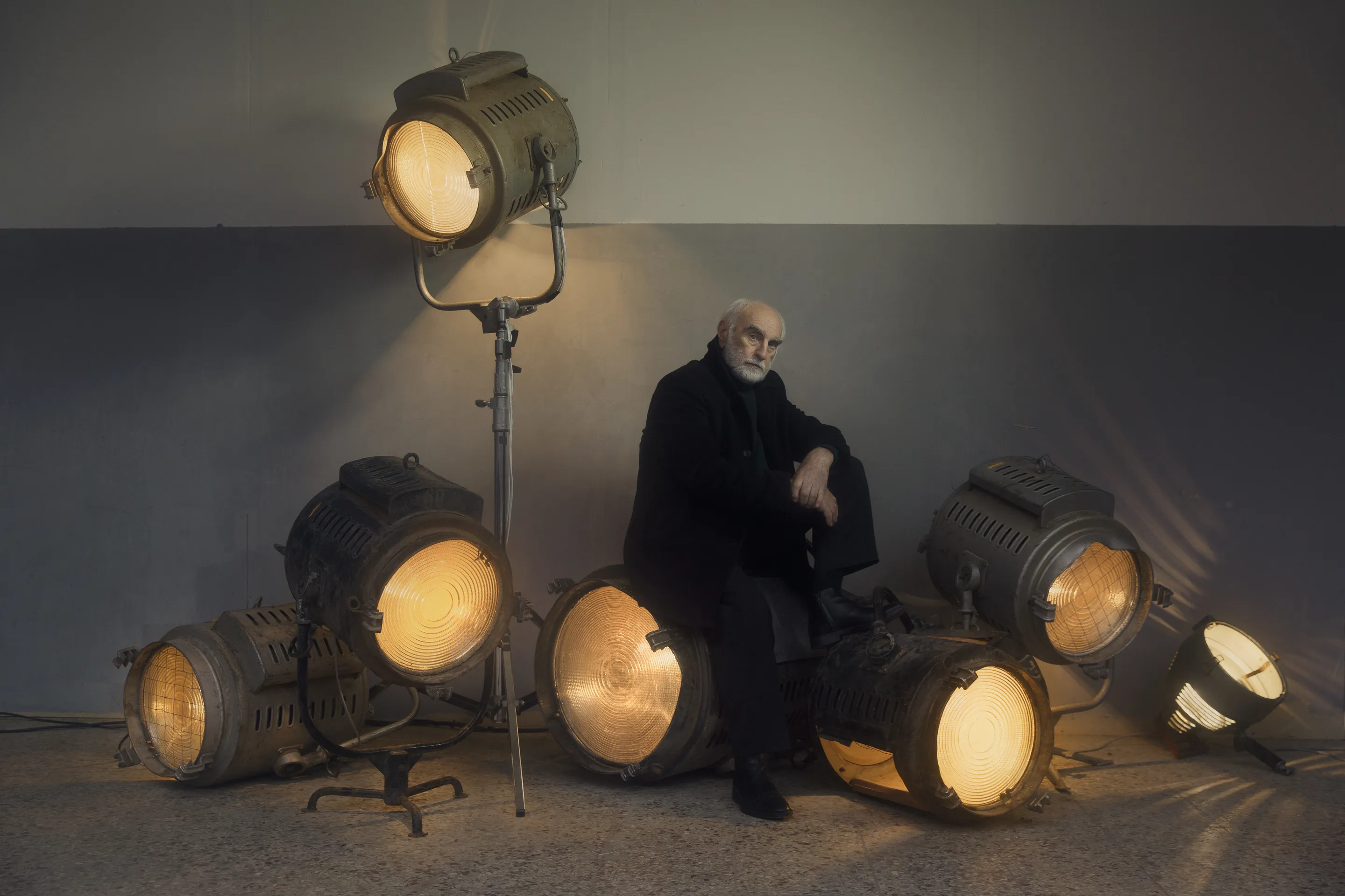 Photograph by Andrei Kovalev: an elderly man sits on the floor among vintage studio spotlights.